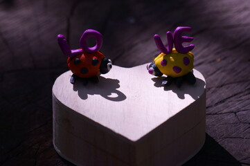 Canvas Print - Two ladybugs made of plasticine on a wooden box in the form of a heart. Next to it is the inscription love.