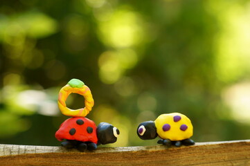 Poster - Two ladybugs made of plasticine on a colored background. Next to it is a ring made of plasticine.