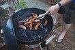 © Natalie Jeffcott/Stocksy - Man grilling sausages on kettle bbq with coal / charcoal