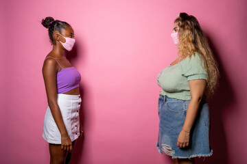 Two young women black and caucasian respecting social distancing wearing mask - Isolated diverse women posing 6 feet away wearing face mask - protection, prevention concept