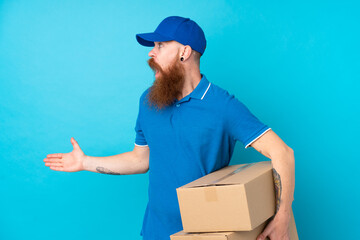 Redhead delivery man over isolated blue background with surprise facial expression