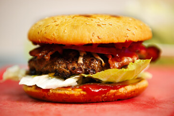 Burger with beef patty & bacon strips prepared for dinner in kitchen on cutting board.American fast food dish cooked on grill in diner cafe