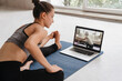 © Arsenii - Fit woman in sportswear doing yoga on exercise mat at home using laptop watching tutorial. Female coach has a virtual yoga class on computer. Healthy and active lifestyle concept. Online home training