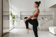 © Arsenii - Young handsome sporty woman in sportswear doing stretching and balancing yoga exercise at home in living room. How to stay healthy on quarantine concept. Fitness, work out, healthy lifestyle concept