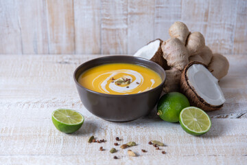 pumpkin cream soup in asian style with ginger and coconut milk on a white wooden table