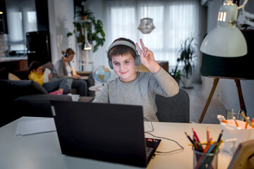 Cute boy with headphones using laptop computer for online learning. Home school. Child doing homework at home. Lifestyle concept for home schooling. Social distancing and education.