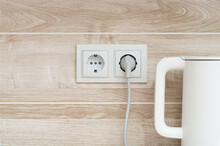 White Electric Power Sockets On Wall Background With Plugged Electric Kettle Into A Kitchen, Copy Space.