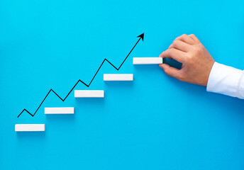 Businessman hand arranging wood block stacking as step stair with growth arrow. Business  growth success and development concept.