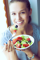 Wall Mural - A beautiful girl eating healthy food, sitting near window