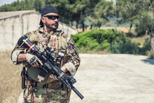 Navy SEALs Fighter In Ballistic Goggles, Equipped Military Ammunition And Body Armour, Holding Service Rifle, Looking In Camera While Standing Outdoors. Special Forces Soldier Half-length Portrait