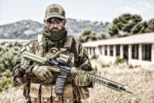 Private Military Company Mercenary, Brutal Looking Special Forces Fighter In Battle Uniform And Plate Carrier, Wearing Radio Headset And Sunglasses, Holding Service Rifle In Hands, Ready To Fight