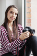 © W2 Photography/Stocksy - Young woman sitting in a window with camera.