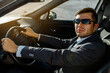 © Med Photo Studio - man businessman in a jacket, shirt, tie and sunglasses is driving a car.