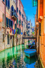 Wall Mural - Venice cityscape with narrow water canal with boats moored between old colorful buildings and bridge, Veneto Region, Northern Italy. Typical Venetian view, vertical view, blue sky background