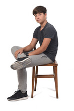 Side View Of Teenage Boy Sitting On A Chair With White Background,looking At Camera