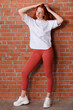 © oleg_ermak - Fashion style studio portrait of beautiful red-haired young girl in leggings pants and white t-shirt. Model standing and posing beside brick wall