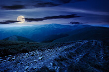 Mountain Road Through Grassy Meadow At Night. Wonderful Summer Adventure In Full Moon Light. Clouds On The Blue Sky