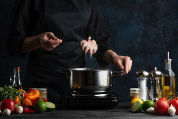 The chef in black apron cooking baby octopus on the professional kitchen. Chef's hand putting seafood into the pot with boiling water. Food concept.