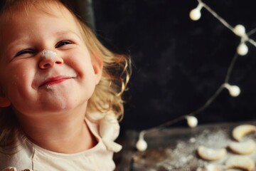 Portrait of a beautiful child 2-3 years old. Baby is preparing New Year and Christmas cookies. Food and baby in the frame. A child sprinkles cookies with powdered sugar. Happy childhood. Baby smile