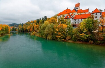 Wall Mural - Fall scenery of beautiful Lech River with the majestic landmark architecture, Hohes Schloss Castle, in the background and colorful autumn trees by the riverside, in Fussen, Bavaria, Germany, Europe