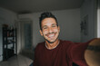 © Davide Angelini - Happy young handsome millennial taking a selfie smiling at the camera in the living room at home.