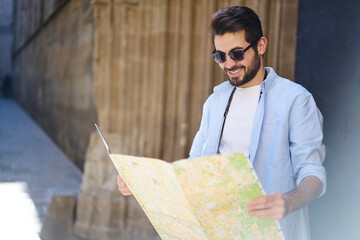 Wall Mural - Cheerful young man standing with map in shadow on street