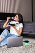 © F8  \ Suport Ukraine - Young woman eating sushi look at her laptop sitting on the floor at bed working at home