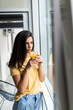 © F8  \ Suport Ukraine - Young nice woman smiling and drinking fresh juice while standing near window indoors