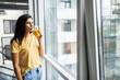 © F8  \ Suport Ukraine - Young nice woman smiling and drinking fresh juice while standing near window indoors