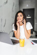 © F8  \ Suport Ukraine - Attractive young woman working on laptop and talking on the phone while sitting in the kitchen