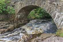 The Old Bridge Of Dochart, Where The River Dochart Flows Through The Village Of Killin In The Highlands Of Scotland, Near The Area Of Waterfalls And White Water Rapids Known As The Falls Of Dochart.
