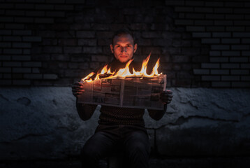 a guy reads a burning newspaper against a dark wall, the concept of burning news,