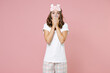 © ViDi Studio - Shocked young brunette woman in white pajamas home wear sleep mask cover mouth with hands while resting at home isolated on pastel pink background studio portrait. Relax good mood lifestyle concept.