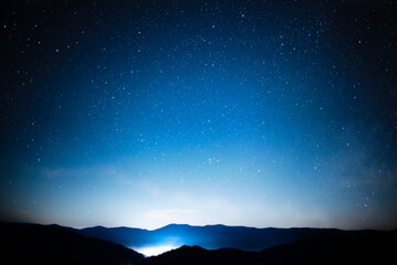 Wall Mural - starry sky over mountains panorama with city lights below
