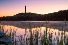 Tall Obelisk Monument On A Mountain Reflecting In Still Water At Sunrise. High Point State Park, New Jersey
