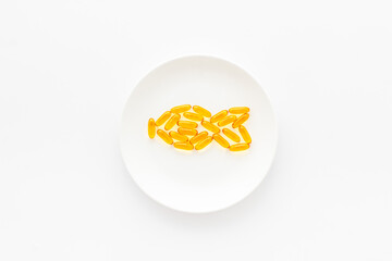 Wall Mural - Omega cod liver oil capsules on plate with fish shape, top view