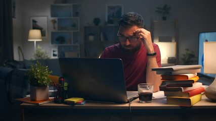 Young man rubbing eyes with fatigue at midnight at home in living room while studying