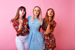 ©  AnnaHar - Bright positive portrait of three happy hipster woman having fun and sending air kisses to camera, color matching summer clothes and colorful sunglasses, pink background, youth girls party.