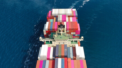 Aerial drone photo of huge container cargo Ship carrying load in truck-size colourful containers cruising deep blue open ocean sea 