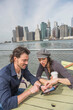 © Tetra Images - Happy couple sitting and using tablet pc with cityscape in background