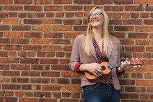 Woman Standing Against Brick Wall And Playing Ukulele