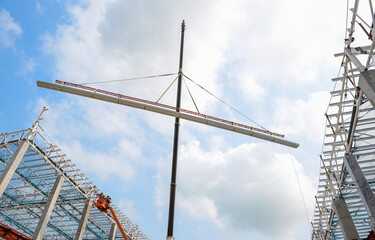 Mobile crane lifting metal roof sheet on palate truss up to stock above steel structure roof truss at the construction site project