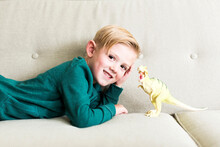 Boy (2-3) Lying On Sofa With Toy Dinosaur