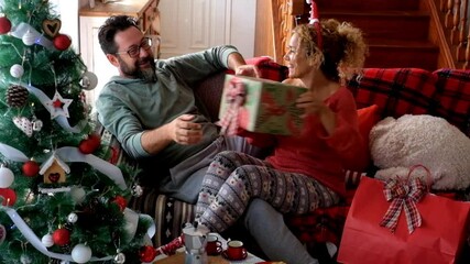 Wall Mural - Gift surprise scene with happy adult couple at home during Christmas Eve day - happy man after receive a big red presents from his wife girlfriend - bored man become joyful during holidays