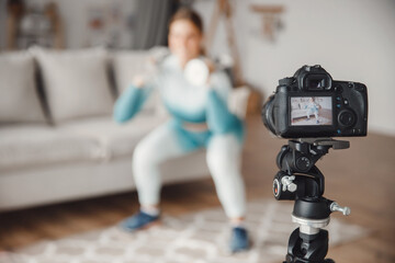 Video recording of online sports training on camera, woman performs fitness exercises home on background of kitchen