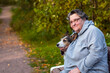 Portrait of a senior citizen hugging her dog in the park on a bench. Old woman walks with her pet in autumn in the park