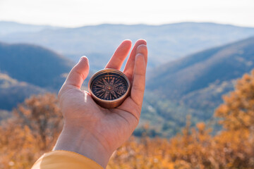 Female hand of traveler, hiker with compass on background autumn forest landscape with mountains on the horizon in orange colors in fall.