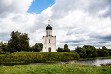 Wall Mural - snow-white stone old church against the background of a green meadow and lake before a summer thunderstorm