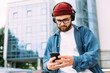 © mykolastock - Young bearded hipster man in headphones using smartphone and having video chat.