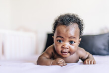 Adorable African-American Baby Lying In Bed And Smiling